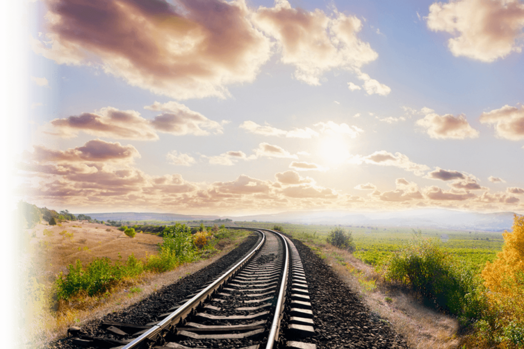 View down an empty railroad track with clouds and sun ahead