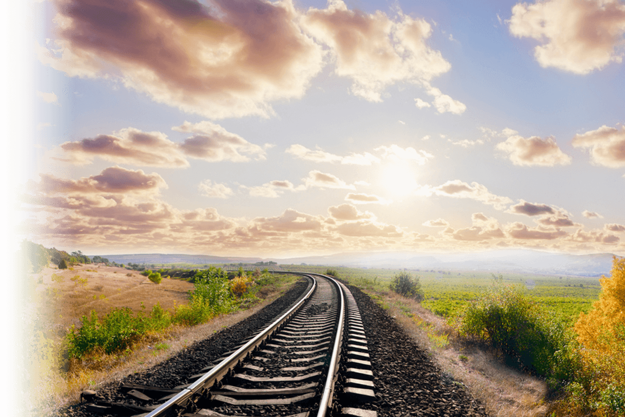 View down an empty railroad track with clouds and sun ahead